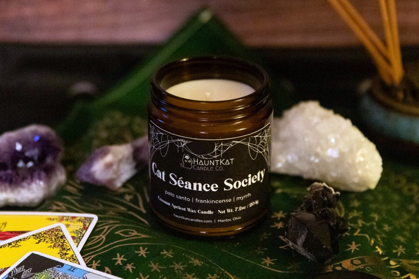Candle jar labeled 'Cat Séance Society' on a mystical-themed surface with crystals and tarot cards.