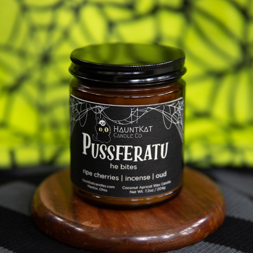 Amber jar candle named 'Pusseratu' on a wooden stand with a colorful, spiderweb background