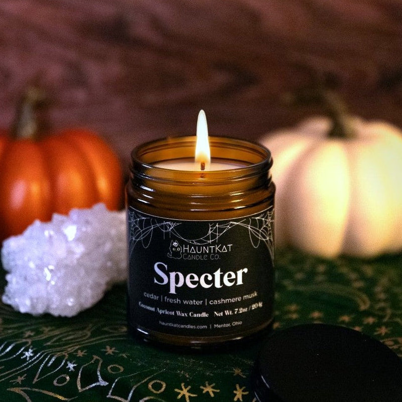 Candle in a jar labeled 'Specter' with pumpkins and decorative stones in the background